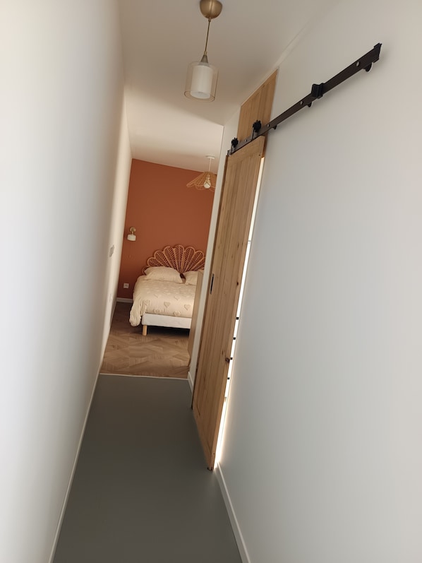 A narrow hallway leading to a bedroom with a bed and a wooden wardrobe.
