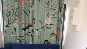 Ett rum med en blå soffa, blommiga gardiner och en vit vägg med en termostat.