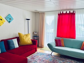 A living room with a red sofa, a teal sofa, and a floor lamp. - Flumser-Höckli - Casa Lilly (CharmingStay), (Flumserberg Tannenheim), by Interhome (Flumserberg Tannenheim)