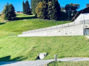 A grassy slope with a concrete retaining wall and a metal fence. - Flumser-Höckli - Casa Lilly (CharmingStay), (Flumserberg Tannenheim), by Interhome (Flumserberg Tannenheim)