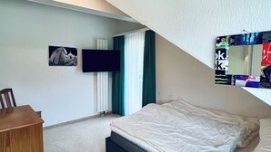 A bedroom with a bed, a desk, a television, and a window with curtains.