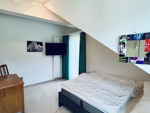Una camera da letto con un letto, una scrivania, una televisione e una finestra con tende.