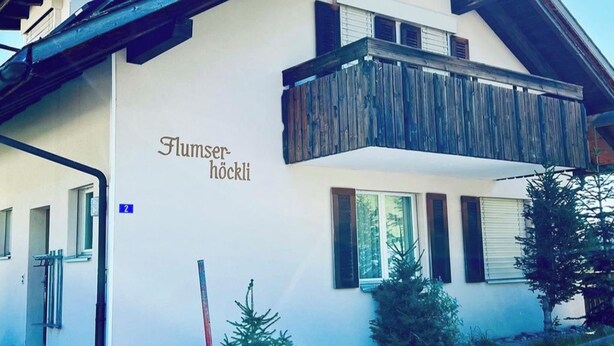 A two-story building with a balcony and a sign that reads 'Flumsser nocki'.