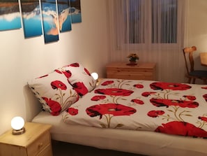 Un dormitorio con cama, mesita de noche, cómoda de madera y una silla.