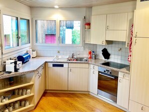 Eine kleine Küche mit Geschirrspüler, Backofen und einem Fenster mit Jalousien.
