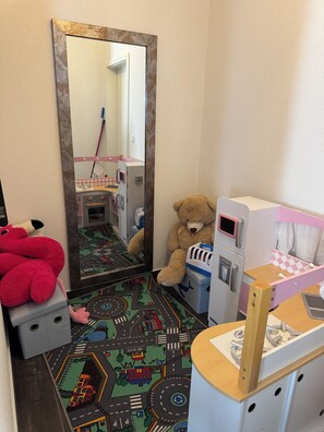 A child's playroom with a large mirror, a teddy bear, and a toy kitchen set.