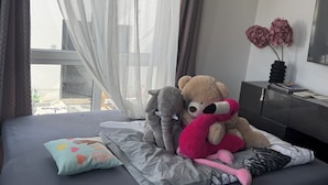 Un lit avec un matelas gris, un oreiller coloré et un ours en peluche.
