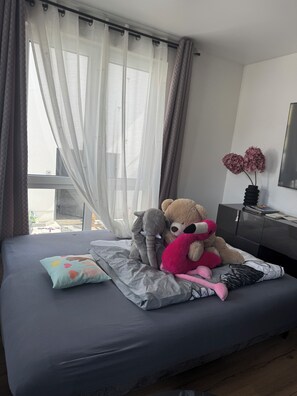 Uma cama com colchão cinza, travesseiro colorido e um urso de pelúcia.