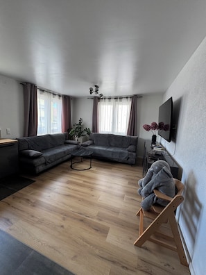 Uma sala de estar moderna com um sofá seccional, uma mesa de centro de madeira e uma televisão fixada na parede.