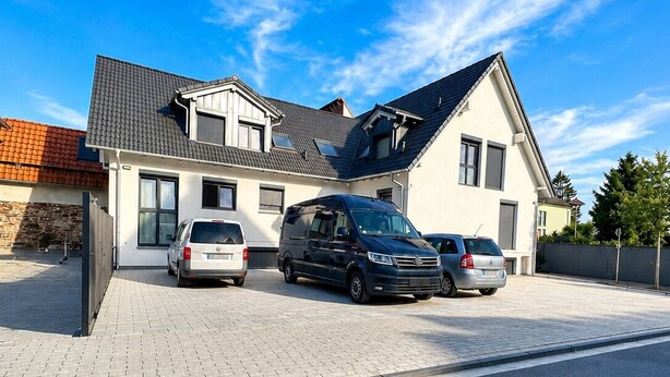Une maison moderne à deux étages, dotée d’une allée pavée où sont garées deux voitures.