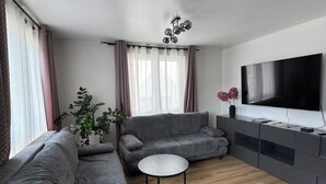 Un salon moderne avec un canapé gris, une table basse ronde, un téléviseur à écran plat et une plante en pot.