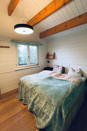 Ein Schlafzimmer mit einem Bett, einem Fenster, einer Pendelleuchte und Holzbalken an der Decke.
