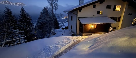 Un paysage montagneux enneigé, avec une maison située au pied d’une pente.