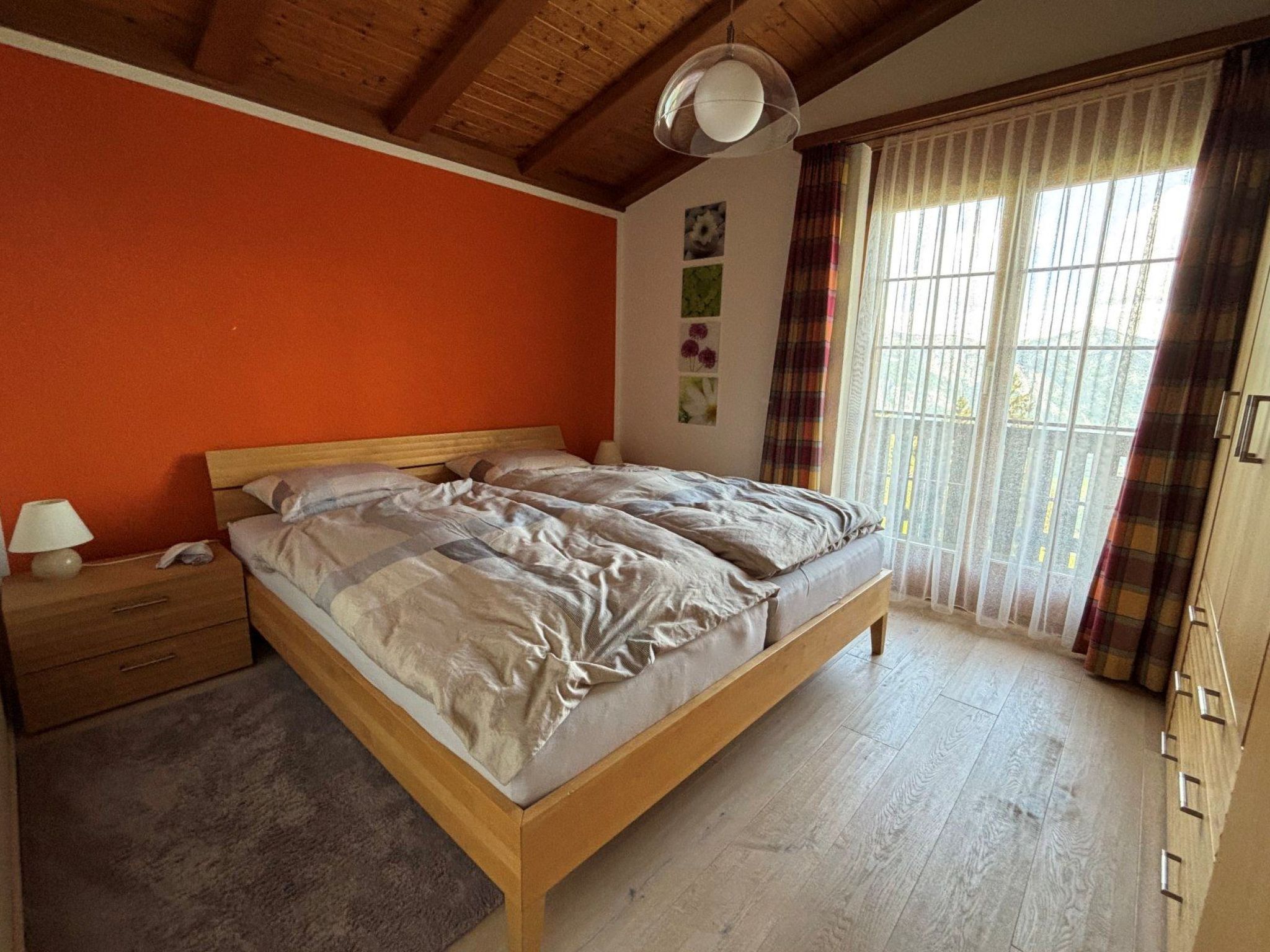 A bedroom with a wooden bed, a nightstand, a lamp, and a window with curtains.