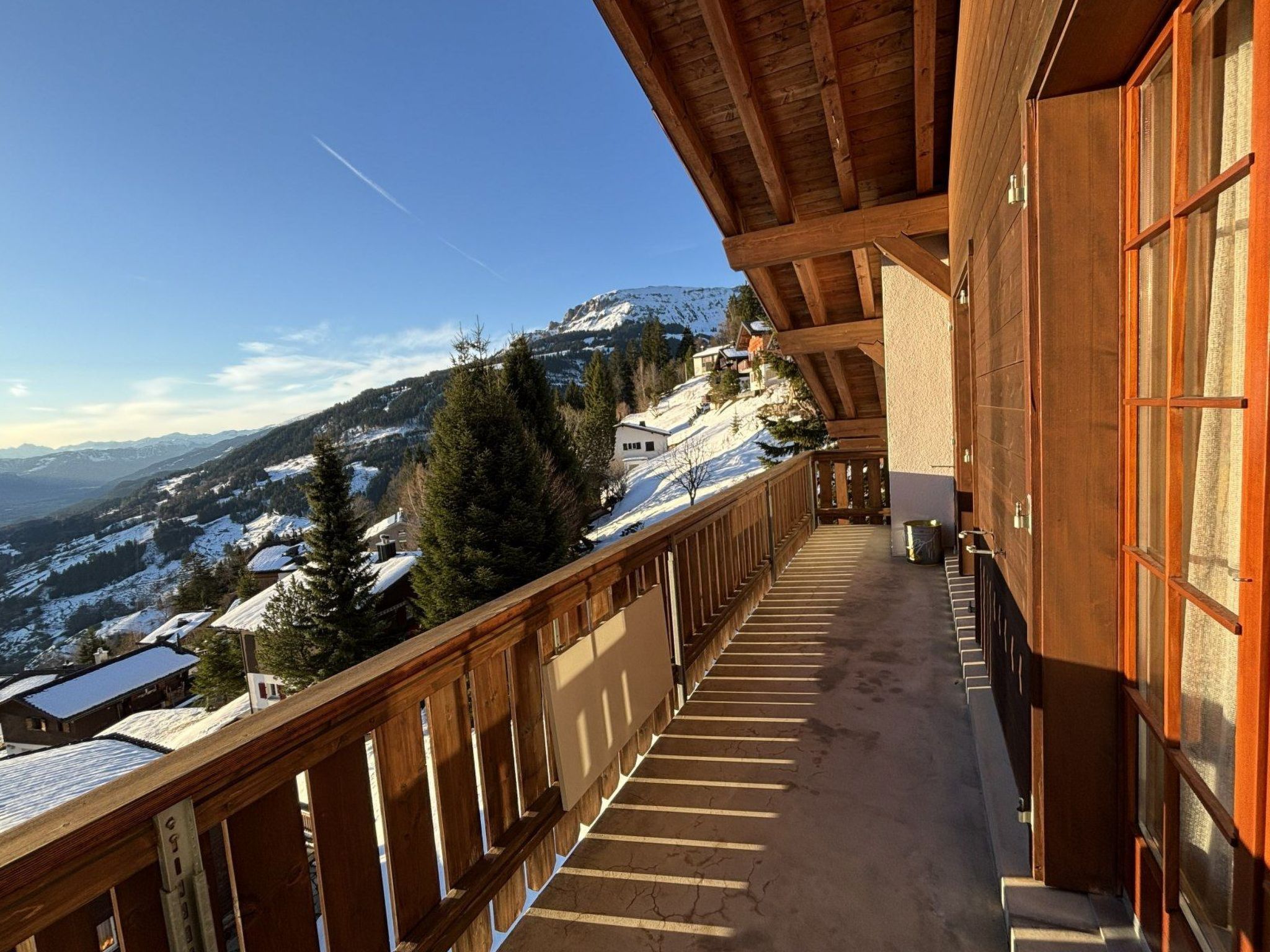 A wooden balcony with a view of snow-covered mountains and houses.