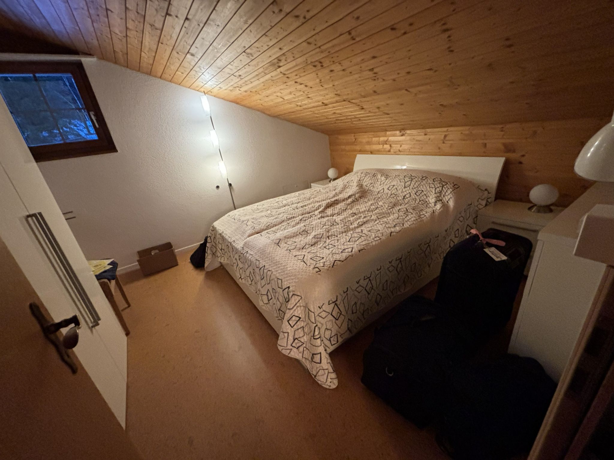 Een slaapkamer met een bed, een nachtkastje, een lamp en een raam.