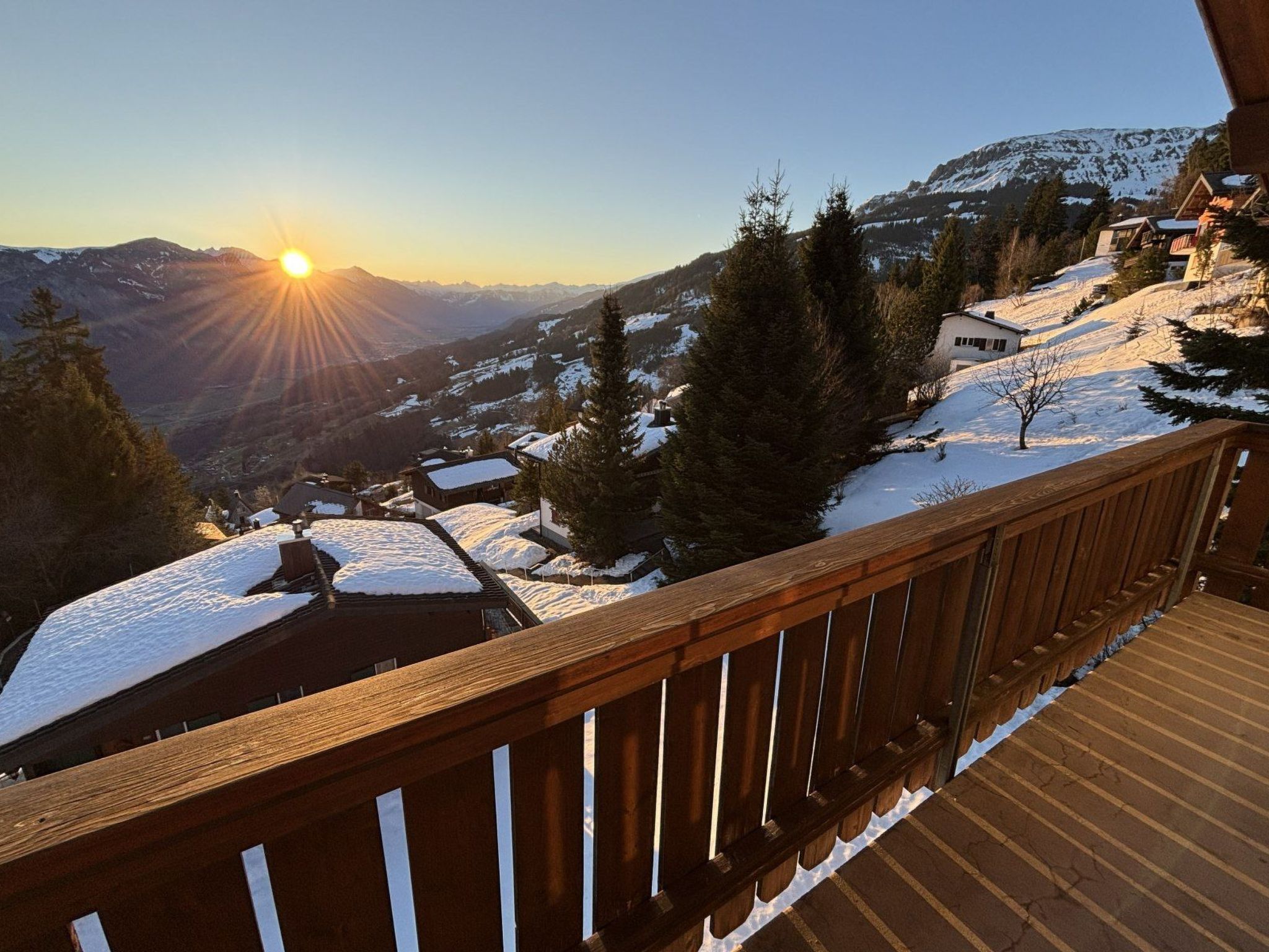 A wooden deck overlooking a snowy landscape with a view of mountains and a clear sky.