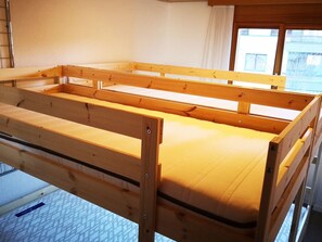 A wooden bunk bed with a mattress, metal frame, and a window with curtains.