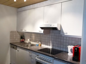 A modern kitchen with white cabinets, a stainless steel sink, a built-in oven, and a black stovetop.