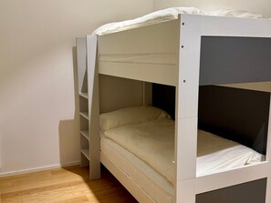 En våningssäng med en stege på vänster sida, en enkelsäng på höger sida och ett trägolv.
