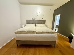 A bedroom with a bed, a nightstand, a wall-mounted lamp, and a window. - Bergträume Haus Gauen (CharmingStay), (Flumserberg Tannenheim), by Interhome (Flumserberg Tannenheim)