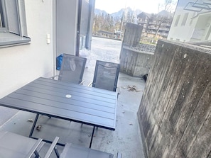 An outdoor patio with a table and chairs, a concrete wall, and a view of buildings and trees in the background. - Bergträume Haus Gauen (CharmingStay), (Flumserberg Tannenheim), by Interhome (Flumserberg Tannenheim)