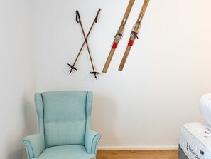 Ett rum med en ljusblå fåtölj, en säng med en vit madrass och två par skidor som hänger på väggen.