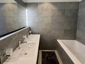 A modern bathroom with a large bathtub, a double sink vanity, and a mirror. - Bergträume Haus Gauen (CharmingStay), (Flumserberg Tannenheim), by Interhome (Flumserberg Tannenheim)