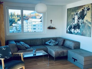 A modern living room with a large window, a sofa, a coffee table, and a painting on the wall. - Panorama View (CharmingStay), (Flumserberg Tannenbodenalp), by Interhome (Flumserberg Tannenbodenalp)