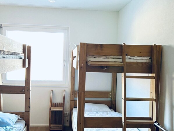 A bunk bed room with a window, a chair, and a door.
