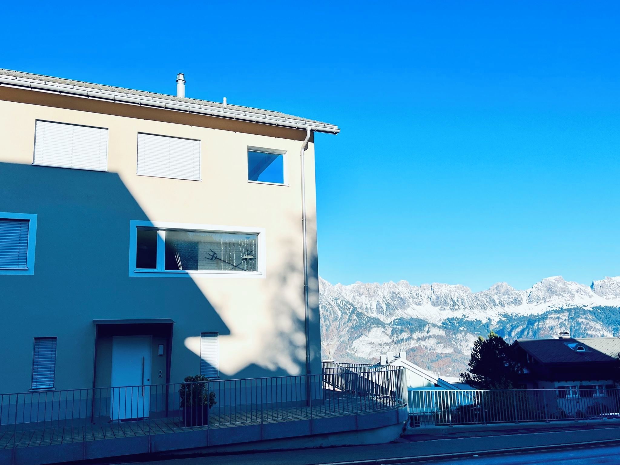 Un bâtiment à deux étages doté d’un balcon, d’une fenêtre avec une antenne de télévision et ayant une chaîne de montagnes en arrière-plan.