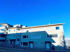 A multi-story residential building with a flat roof, multiple windows, and a visible balcony on the left side. - Panorama View (CharmingStay), (Flumserberg Tannenbodenalp), by Interhome (Flumserberg Tannenbodenalp)