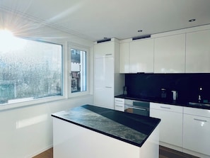 A modern kitchen with white cabinets, a black countertop, and a window providing a view of the outside. - Panorama View (CharmingStay), (Flumserberg Tannenbodenalp), by Interhome (Flumserberg Tannenbodenalp)