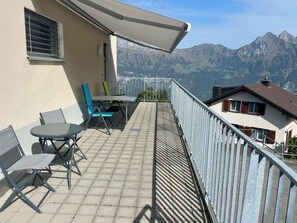 Ein Balkon mit Tisch und Stühlen, Blick auf Berge und ein Gebäude mit geneigtem Dach.