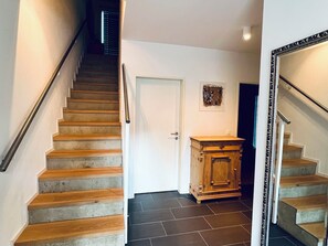 Eine Treppe mit Holzbodenstufen und einem Metallgeländer, die zu einer Tür führt, neben der sich ein kleines Schranks steht.