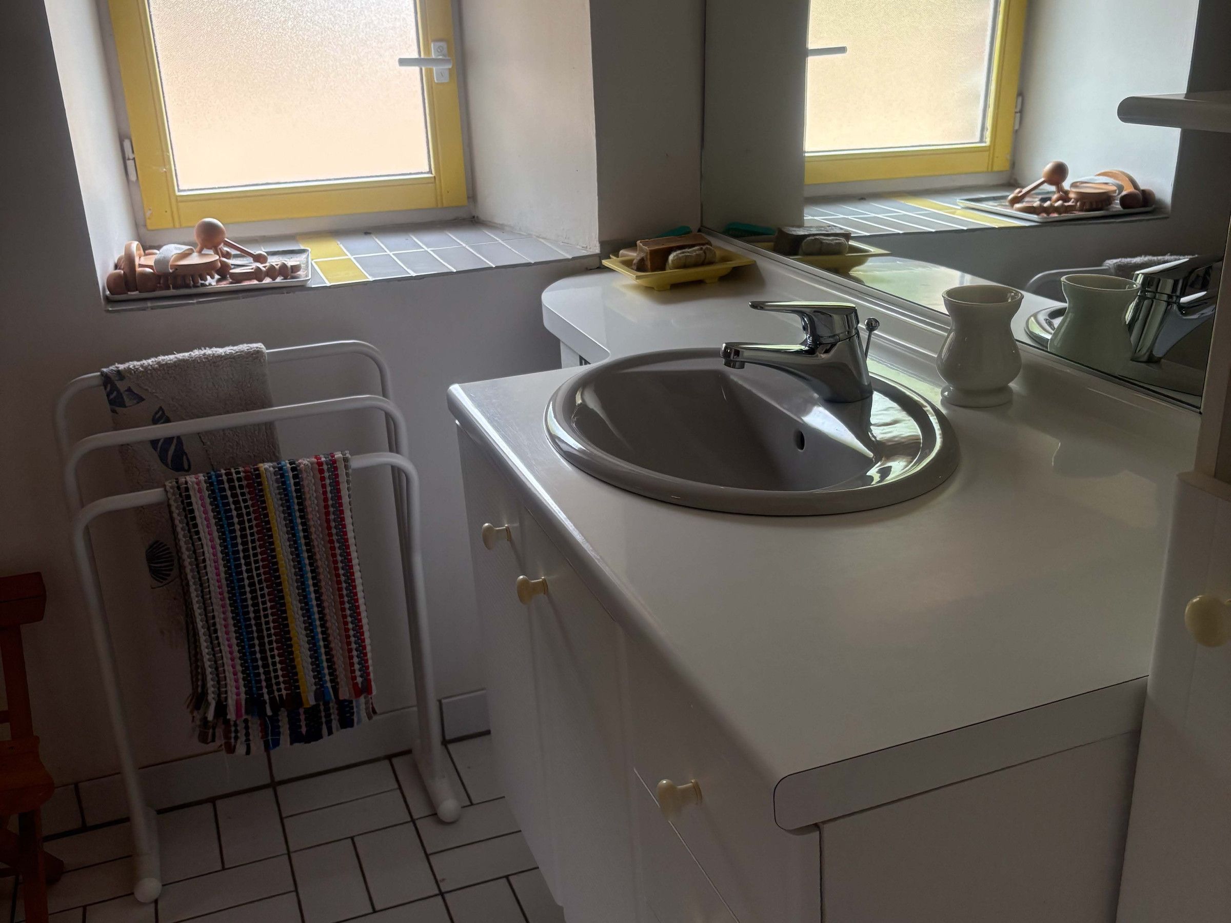 A bathroom with a white sink, a towel rack with a colorful towel, and a window with a view.