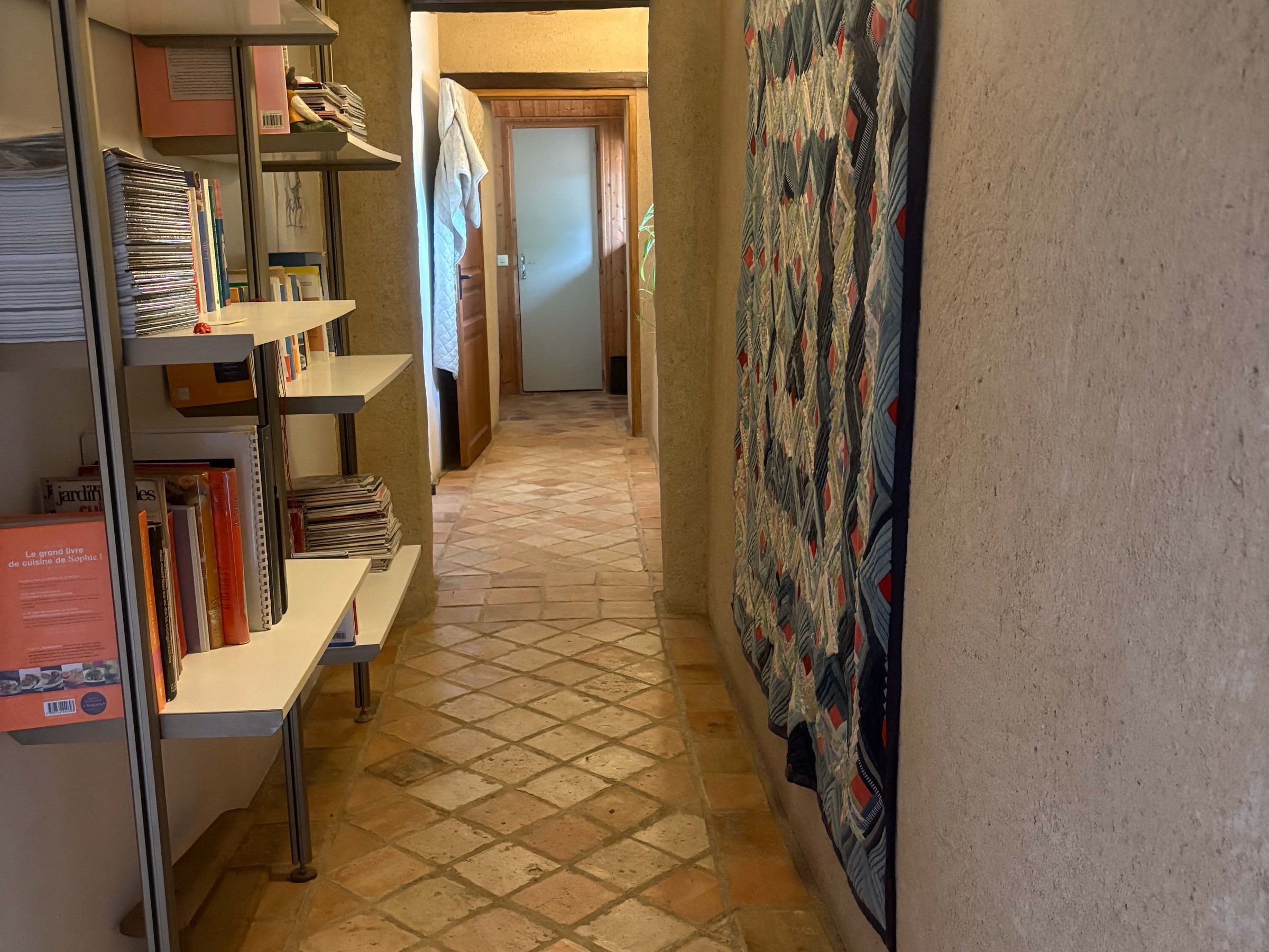 Um corredor com piso de azulejos, uma estante cheia de livros e um painel de parede estampado.