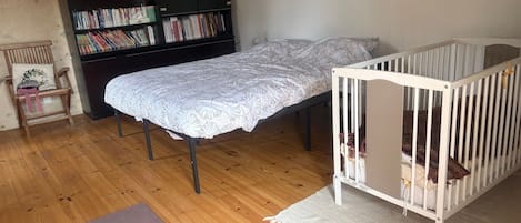Huoneessa on vauvansänky, kuviollinen päiväpeite päällystetty sänky, puulattia, kirjahylly ja pehmustettu tuoli.