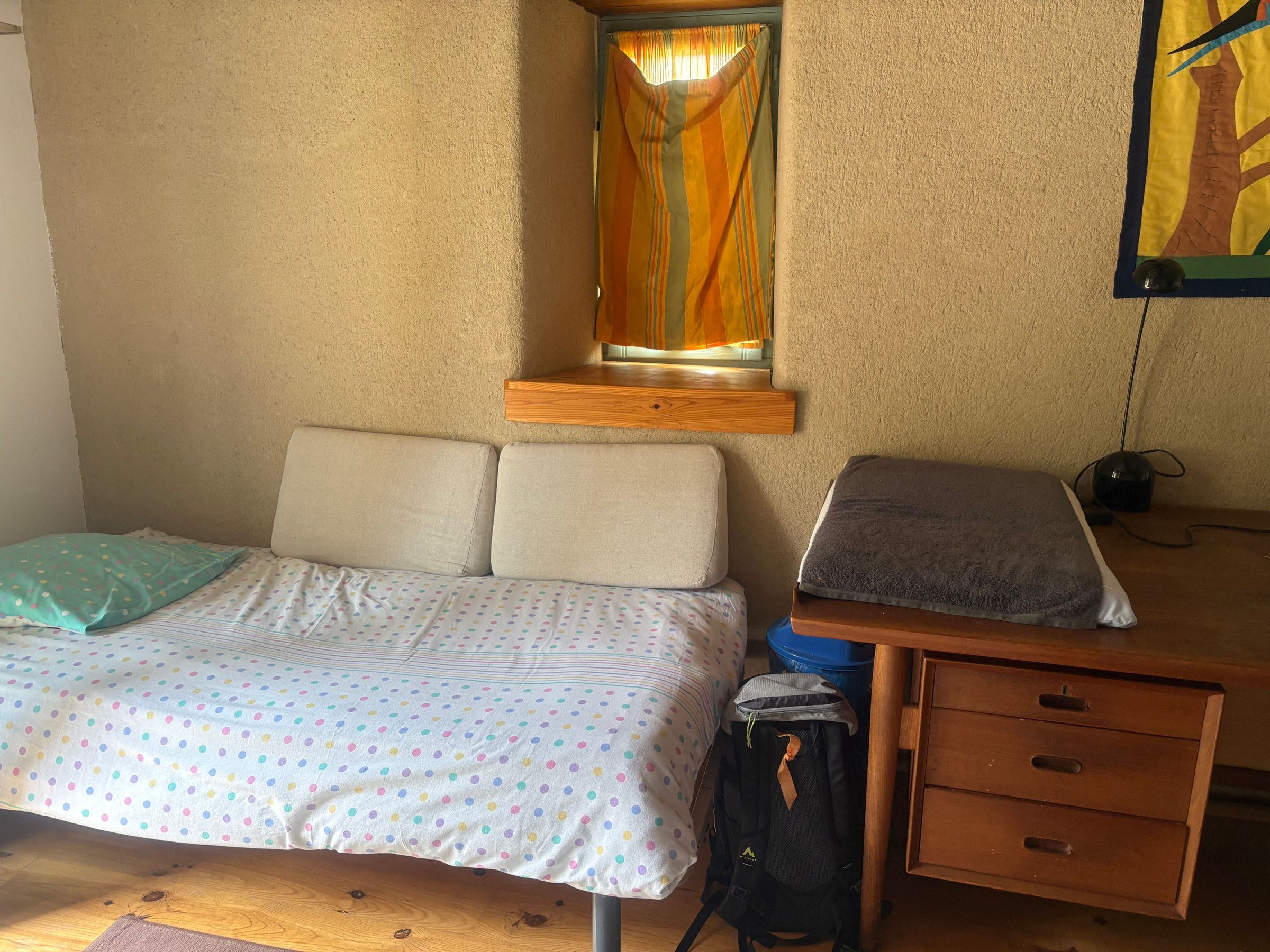 Ein Schlafzimmer mit einem Bett, einem Schreibtisch, einem Stuhl und einem Fenster mit Vorhängen.