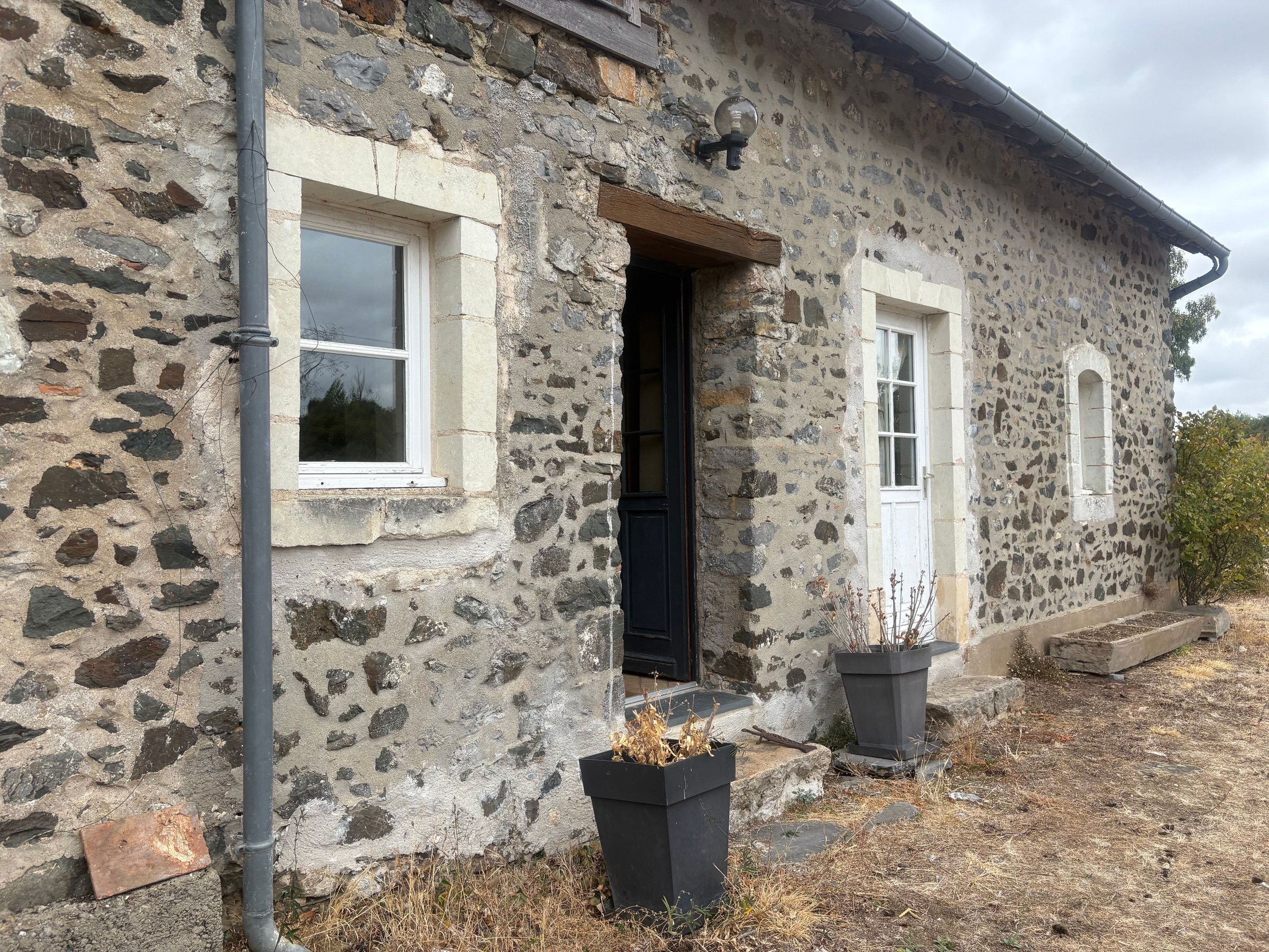 Un edificio de piedra con una puerta negra, dos ventanas y dos macetas negras.