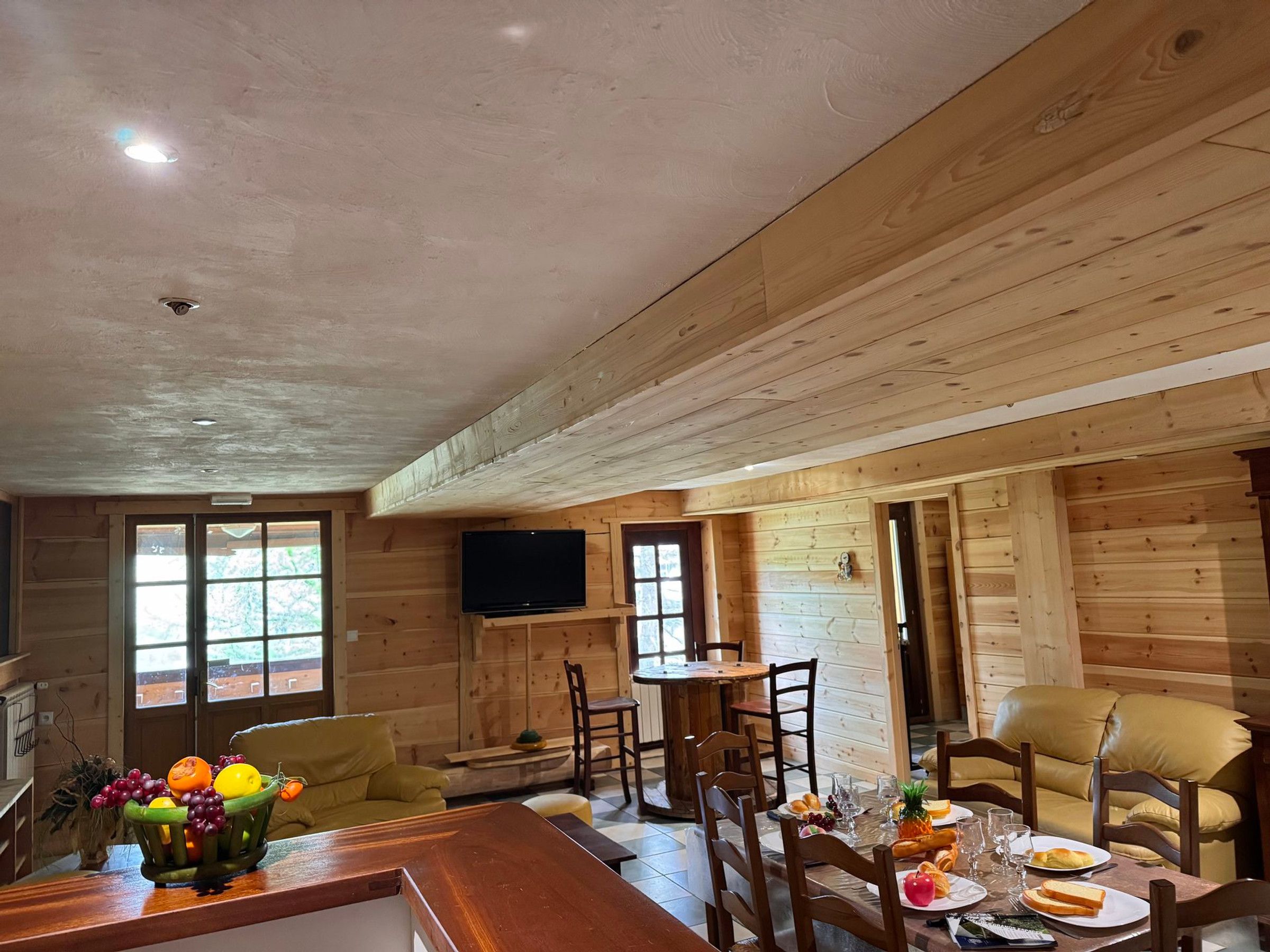 A wooden interior with a dining area, a television mounted on the wall, and a fruit basket on the counter.
