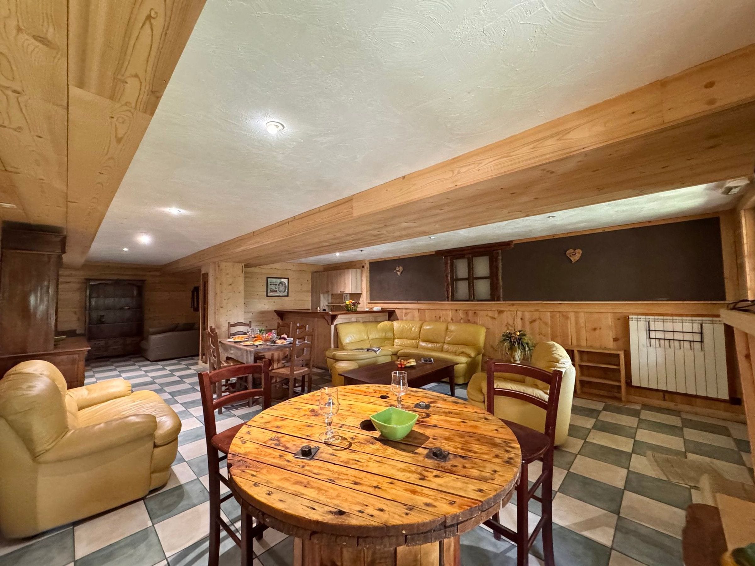 A wooden interior with a round wooden table, leather sofa, and a checkered floor.