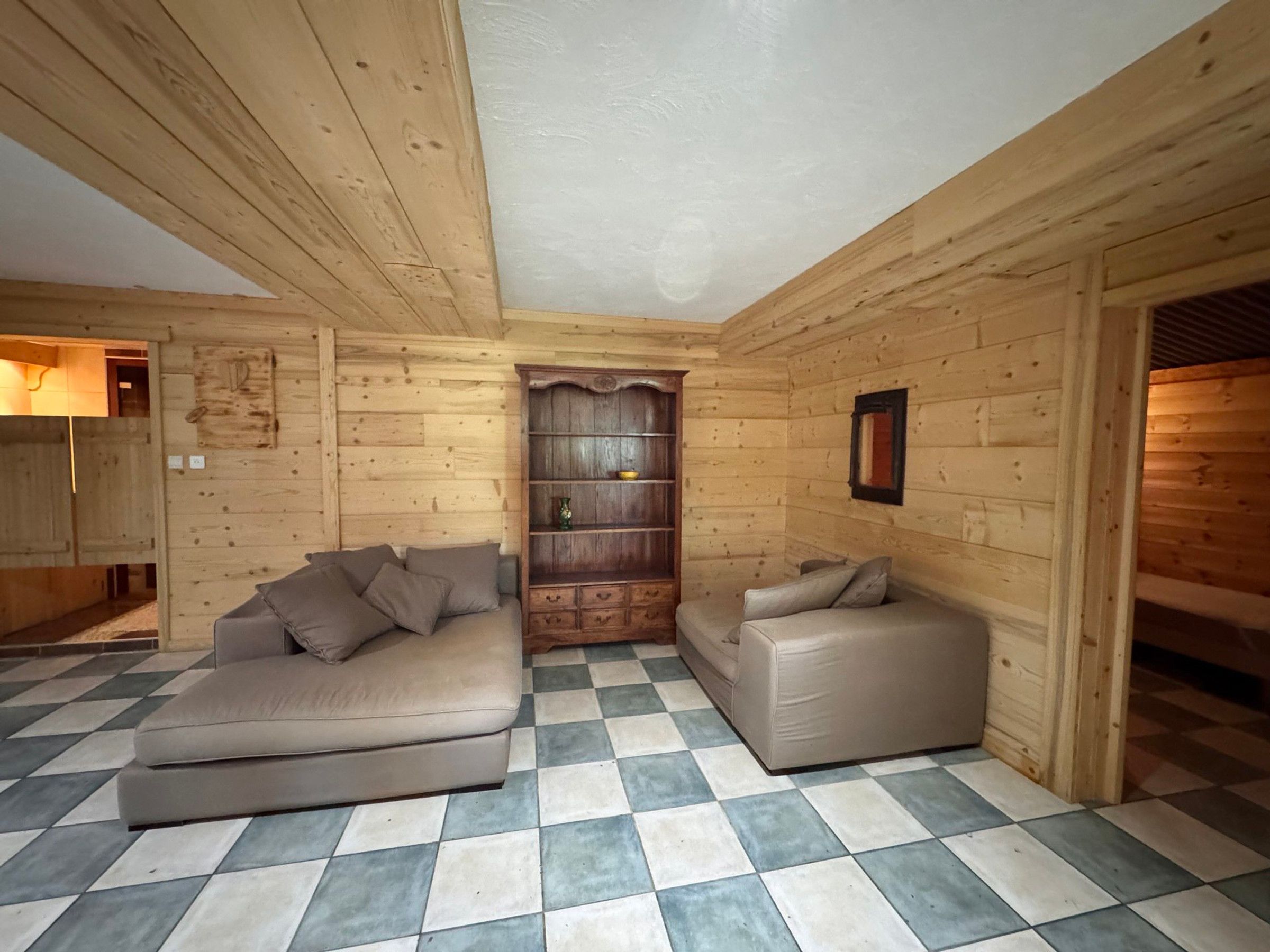 A log cabin interior with a checkered floor, a sofa, a loveseat, and a wooden bookshelf.