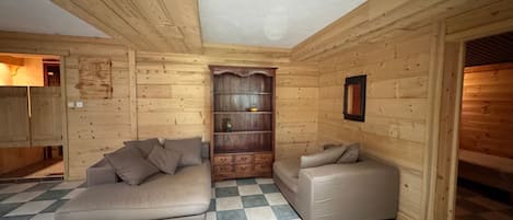 A log cabin interior with a checkered floor, a sofa, a loveseat, and a wooden bookshelf.