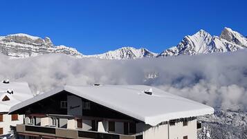 Ein schneebedecktes Berghotel mit Balkon, umgeben von verschneiten Gipfeln und Wolken.