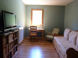 Una habitación con televisión sobre un mueble de madera, un escritorio con una silla, un radiador y un sofá.