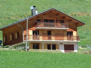 A two-story wooden chalet with a balcony on the upper floor, surrounded by a grassy landscape. - Chalet for 12 in the heart of ArÃªches-Beaufort (Arêches-Beaufort)