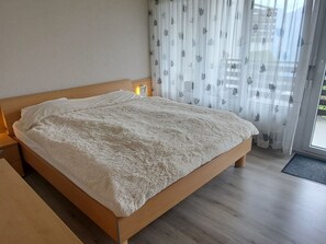 Een bed met een zachte witte deken, een houten hoofdbord en een nachtkastje met een lamp.