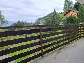 Ein Holzzaun mit Blick auf eine grüne Landschaft, im Hintergrund ein Gebäude.