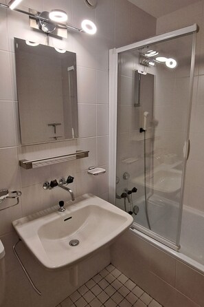 Een moderne badkamer met een douche in een glazen cabine, een wastafel met spiegel erboven en een plank met toiletartikelen.